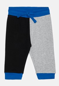 Pantaloni a blocchi di colore, con un lato nero e uno grigio, caratterizzati da una cintura e polsini elastici blu. Realizzati in tessuto morbido e elastico.
