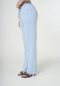 Ljusa blå sammetsträningsbyxor med en mjuk struktur, utrustade med dragsko i midjan, sidfickor och kontrastsömmar.