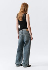 Μαύρο αμάνικο τοπ και άνετο μπλε τζιν παντελόνι. Χαρακτηριστικά περιλαμβάνουν ετικέτα στη μέση, δύο πίσω τσέπες και χαλαρή εφαρμογή.