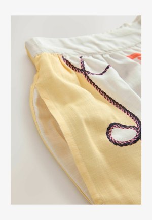 lähivõte kangast pluusist, mis on valmistatud kollasest puuvillast ning mille külgseemel on musta ja roosa köiega tikandid. Kerge ja tekstureeritud.