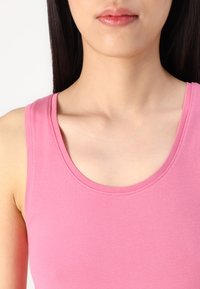 Top sin mangas de cuello redondeado en color rosa, con una textura suave y sedosa y un diseño ajustado, que presenta bordes cosidos y tirantes anchos.