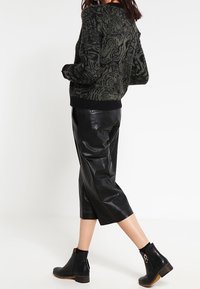 Czarny i zielony sweter w wzory, zestawiony z czarnymi, skórzanymi spodniami o kroju 7/8 oraz botkami na kostkę z jasnobrązową podeszwą i ozdobnym suwakiem.