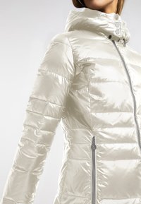 Lichtgewicht, metalen crèmekleurige pufferjack met hoge kraag, ritssluitingen in de zakken en gestikte details voor isolatie en stijl.