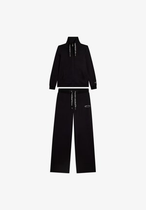 Tuta nera due pezzi con giacca con zip e pantaloni ampi, con lacci bianchi marchiati e piccolo testo bianco su petto e gamba.