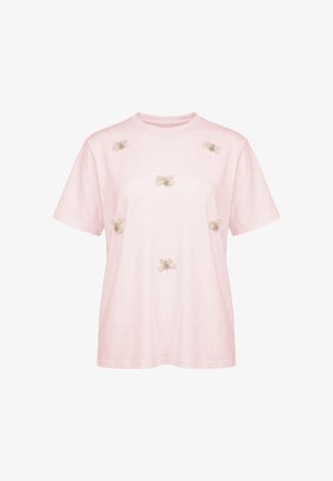 Lys rosa kortærmet T-shirt dekoreret med små blonde-sløjfer jævnt fordelt på forsiden. Ingen synlige logoer eller andre designs.