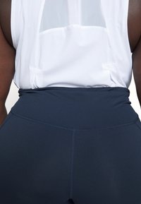 Leggings de talle alto en color azul marino con una textura suave y costuras reforzadas. Combinados con una blusa sin mangas blanca que cuenta con un panel trasero de malla.