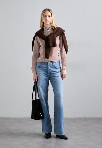 Ραβδωτό πουκάμισο σε μπεζ και μπορντό, συνδυασμένο με ανοιχτό γαλάζιο τζιν με φαρδιά γάμπα. Μπράουν πουλόβερ draped στους ώμους και μαύρη τσάντα.