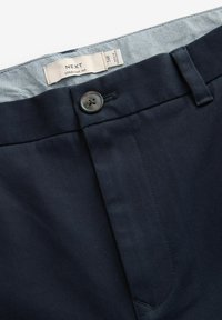 Pantaloni drepti navy cu o textură netedă, închidere cu nasture și un brâu interior cu un model. Eticheta arată informațiile despre marcă și mărime.