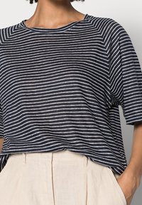 Camiseta de manga corta a rayas en azul marino y blanco con un corte relajado y cuello redondo, combinada con pantalones de cintura alta en color beige.
