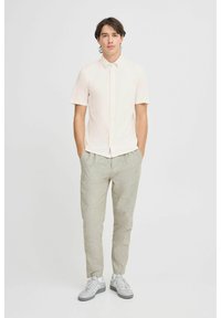 Kortermet, lys rosa skjorte med knapper kombinert med lysegrå linbukser og grå joggesko. Enkel design, avslappet passform, ingen mønstre.
