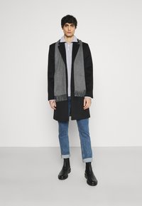 Long black coat with gray scarf, grey pullover, blue jeans, and black ankle boots. Clean lines and a layered look. Smooth fabric textures.