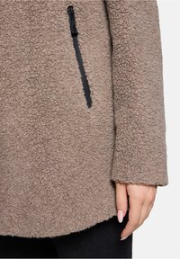 Bruine fleece jas met een gestructureerde stof, zwarte ritszak en een relaxte pasvorm met een afgeronde zoom.