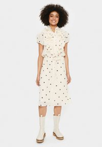 Rochie crem cu gât ruffles și mâneci scurte, av�ând buline negre. Stilizată cu ghete albe până la gleznă și talie cu șnur.