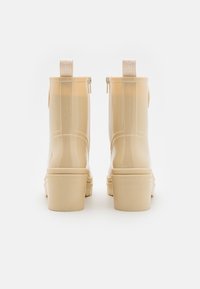 Beige glanzende enkellaarsjes met een ronde neus, blokhak en een trekband aan de achterzijde; gemaakt van een glad synthetisch materiaal.