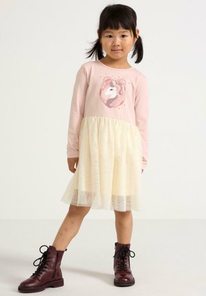 Langdurige jurk met een roze katoen top met een eenhoornafbeelding, en een tule rok in lichtgeel met glitters. Bruine veterschoenen.