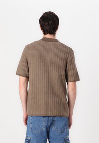 Polo shirt scurt, de culoare maro, cu textura canalată și guler, având o croială relaxată și un design de culoare uniformă.