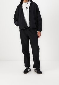 Černá lehká bunda, bílý tričko s potiskem a černé kalhoty. Oblečení doplňují černé tenisky s bílými pruhy.