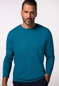 Turkusowa long-sleeve koszulka z okrągłym dekoltem. Posiada subtelne wytłoczone logo na klatce piersiowej oraz gładką, lekką teksturę.