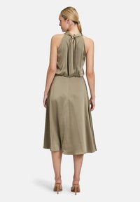 Olivkowa sukienka na ramiączkach z wiązanym tyłem, zwiewna spódnica i gładki, lekki materiał, który elegancko się układa.