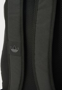 Črni mrežasti nahrbtnik z detajli, ki vključujejo oblazinjene naramnice, teksturirano tkanino in majhen vezen logotip na naramnici.