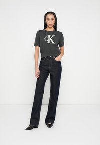 Blugi bleumarin cu croială dreaptă, asortați cu un tricou cu mânecă scurtă gri închis, având un logo alb. Material neted și design minimalist.