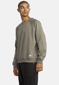 Grijze katoenen sweatshirt met raglanmouwen, ribgebreide manchetten en zoom; voorzien van een klein logopatchje aan de onderkant van de linkerkant.
