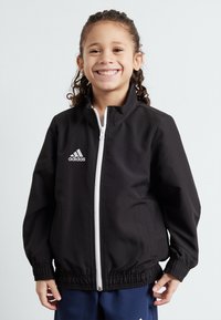 Zwarte sportjack met witte rits en adidas-logo. Bevat elastische manchetten en tailleband, gladde stof en een hoge kraagontwerp.