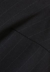 Mustaa kangasta, jossa on hieno viivoituskuvio. Sileä rakenne, keskipaksuus, taitettuna, ja sauman yksityiskohdat näkyvissä.