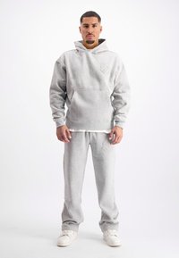 Grijze hoodie met een voorzak en een tonale logo, gecombineerd met bijpassende grijze sweatpants met een soortgelijk reliëfdetail. Witte sneakers.