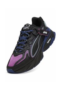 Chaussure de course Puma Nitro noire et violette avec des lacets bleus, une semelle épaisse et une étiquette marquée F1 attachée près du col de la cheville.