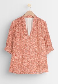Blusa rossa con motivo floreale bianco, scollatura a V e maniche corte a sbuffo. Realizzata in tessuto leggero, presenta una vestibilità comoda.