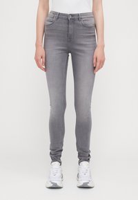 Harmaat slim-fit farkut, joissa on haalistunut pinta, viisi taskua, ommeltuja yksityiskohtia ja nappikiinnitys vyötäröllä, yhdistettynä valkoisiin lenkkareihin.