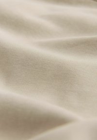 Textile beige avec une texture de tissage fin et homogène. Le tissu semble lisse et doux, mettant en valeur une légère réflexion de la lumière et de douces plis.