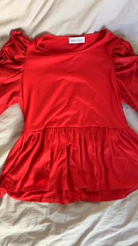 Blusa rossa a maniche corte realizzata in tessuto morbido con un design peplum, caratterizzata da dettagli arricciati sulle maniche e un collo rotondo.