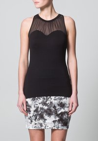 Top negro sin mangas con un escote de malla transparente, combinado con una falda negra y blanca con un patrón que presenta remolinos abstractos y texturas.