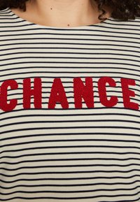 Striped t-shirt in cream and navy. Features bold, textured red "CHANCE" lettering across the chest. Rounded neckline and soft fabric.