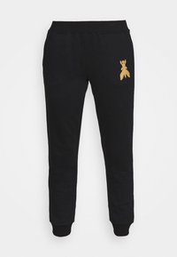 Schwarze Sweatpants aus Baumwollgewebe mit einem goldenen gestickten Design am linken Oberschenkel und gerippten Bündchen an den Knöcheln.
