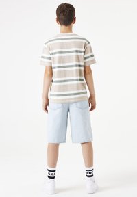 Camisa de manga corta a rayas en beige, verde y blanca; combinada con pantalones cortos de mezclilla azul claro. Zapatillas blancas y calcetas negras completan el conjunto.