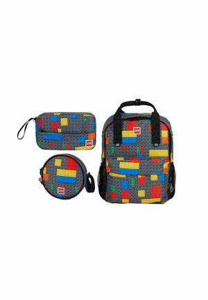 Trois sacs gris avec des motifs colorés de briques LEGO, comprenant un sac à dos, une pochette rectangulaire et un étui rond, tous avec des logos LEGO.