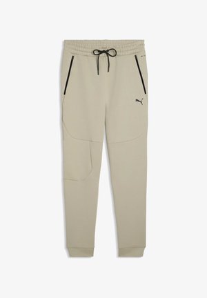 Beige Jogginghosen aus weichem Stoff, mit elastischem Bund und Kordelzug, seitlichen Reißverschlusstaschen und einem kleinen schwarzen Logo am Bein.