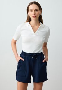 Witte geribde polo met golfrand, gecombineerd met marineblauwe hoge taille shorts met een elastische tailleband en twee voorzakken.
