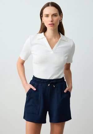 Witte geribde polo met golfrand, gecombineerd met marineblauwe hoge taille shorts met een elastische tailleband en twee voorzakken.