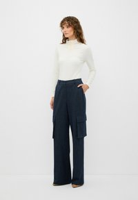 Krämfärgad långärmad topp med strukturerade knappar, kombinerad med marinfärgade randiga vida byxor med cargofickor och en avslappnad passform.