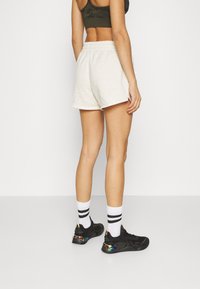 Pantalones cortos de algodón gris claro con cintura elástica, combinados con zapatillas negras y calcetines blancos con dos rayas negras.