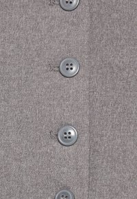 Närbild av ett grått tyg med fyra jämnt fördelade grå knappar sydda i en vertikal linje.