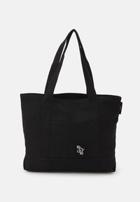 Black canvas tote bag with two sturdy handles, featuring a front pocket and a small logo patch at the lower corner. Simple, functional design.