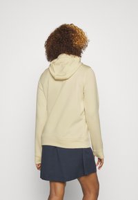 Beige hoodie med en dragsko på huvan, med elastiska mudd och nederkant, i kombination med en marinblå kjol. Slät tygtextur.
