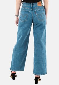 Levi'sin siniset leveälahkeiset farkut, farkkukangasta, korkea vyötärö, näkyvät takataskut ompeludetaljilla, rispaantunut helma, yhdistetty mustien korkokenkien kanssa.