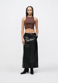 Barna rövidített trikó, fekete bőrmaxi szoknya oldalzsebekkel, sima textúrájú, karcsúsított fazon, fekete magassarkú csizmával. Egyszerű kialakítás.