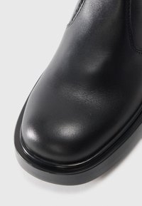 Black leather ankle boot with a smooth texture, rounded toe, and minimal stitching. Features a thick black sole and streamlined design.